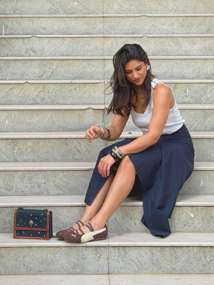 model sitting on steps wearing a white top and navy blue ikami berlin statement skirt with a small bag beside her.