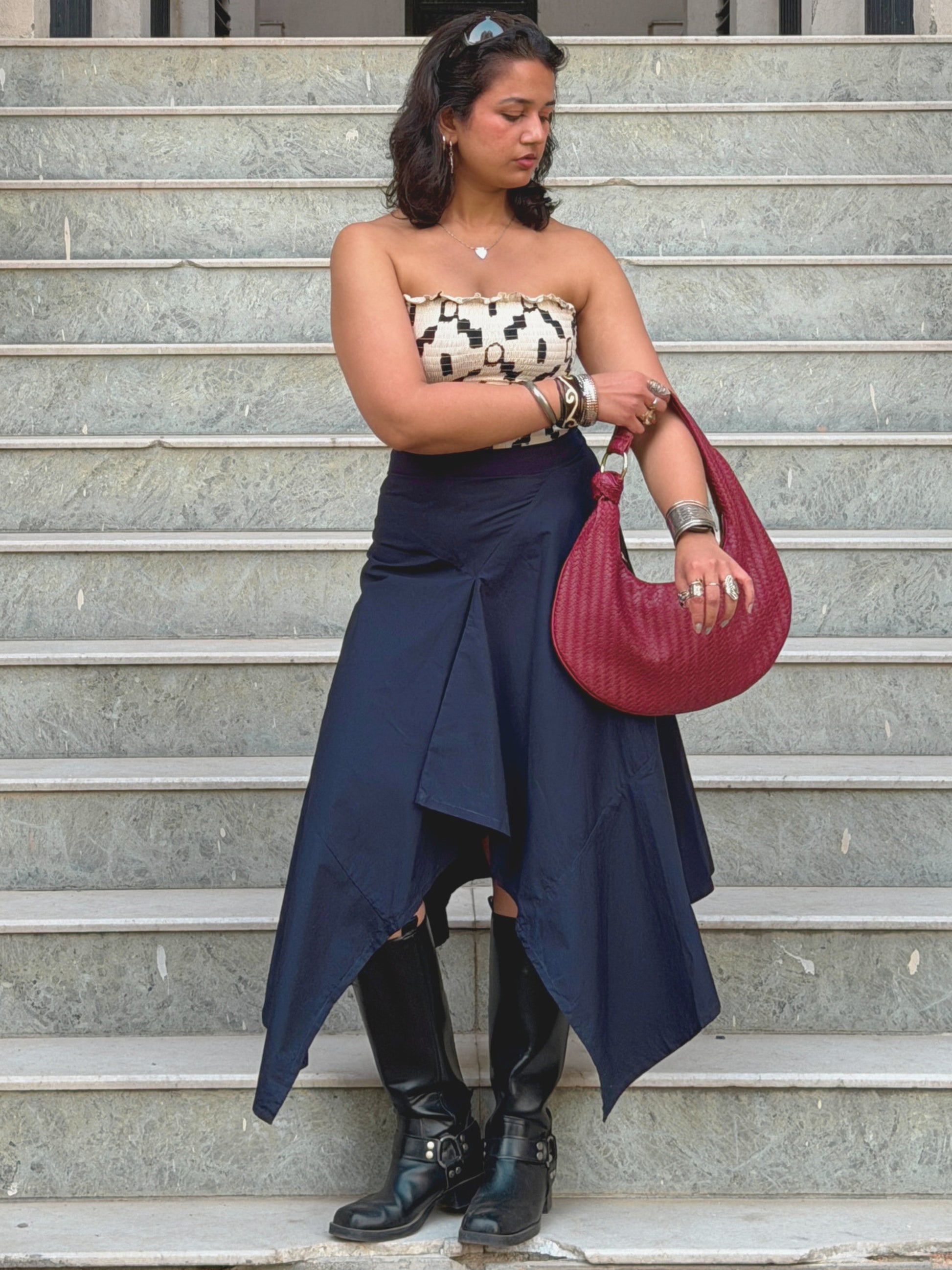 model in strapless top and navy blue ikami skirt holding a red handbag on steps