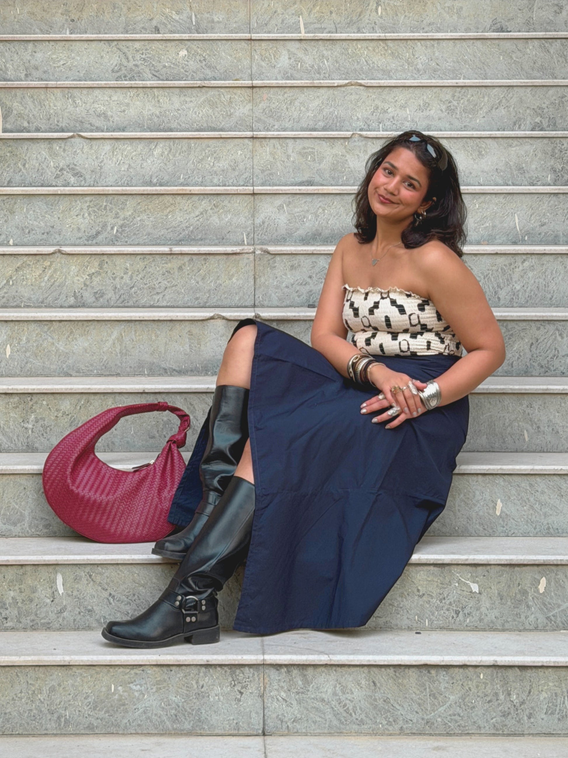 model sitting on steps wearing a strapless top and navy blue ikami berlin skirt with a red handbag