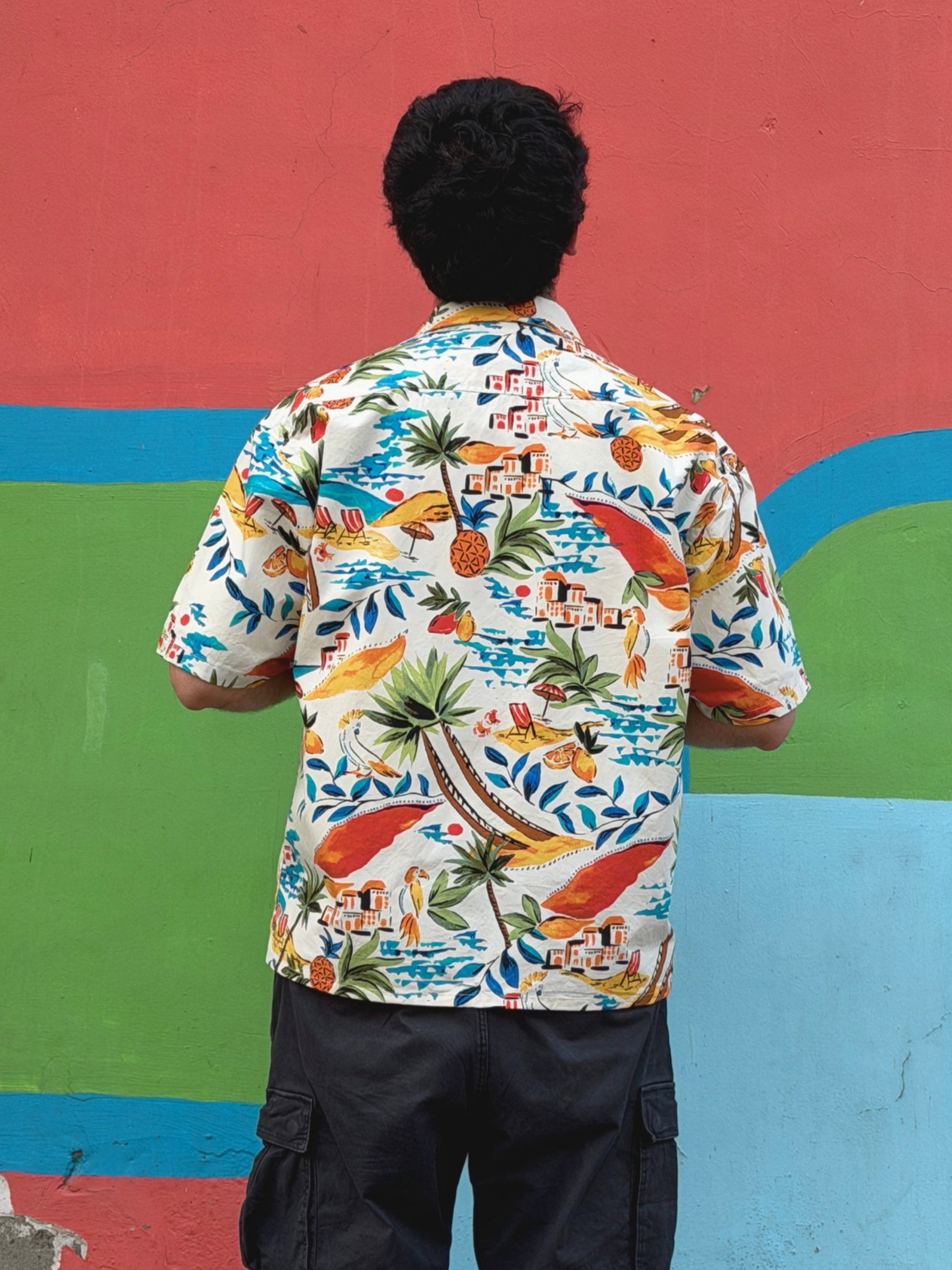 back view of model wearing the colourful ikami mykonos shirt against a multi coloured wall