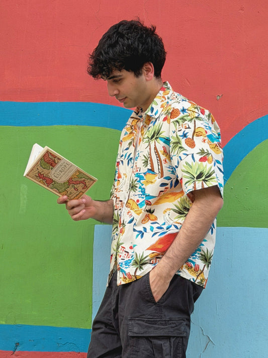 model wearing the colorful ikami mykonos shirt holding a book against a multicolored wall.