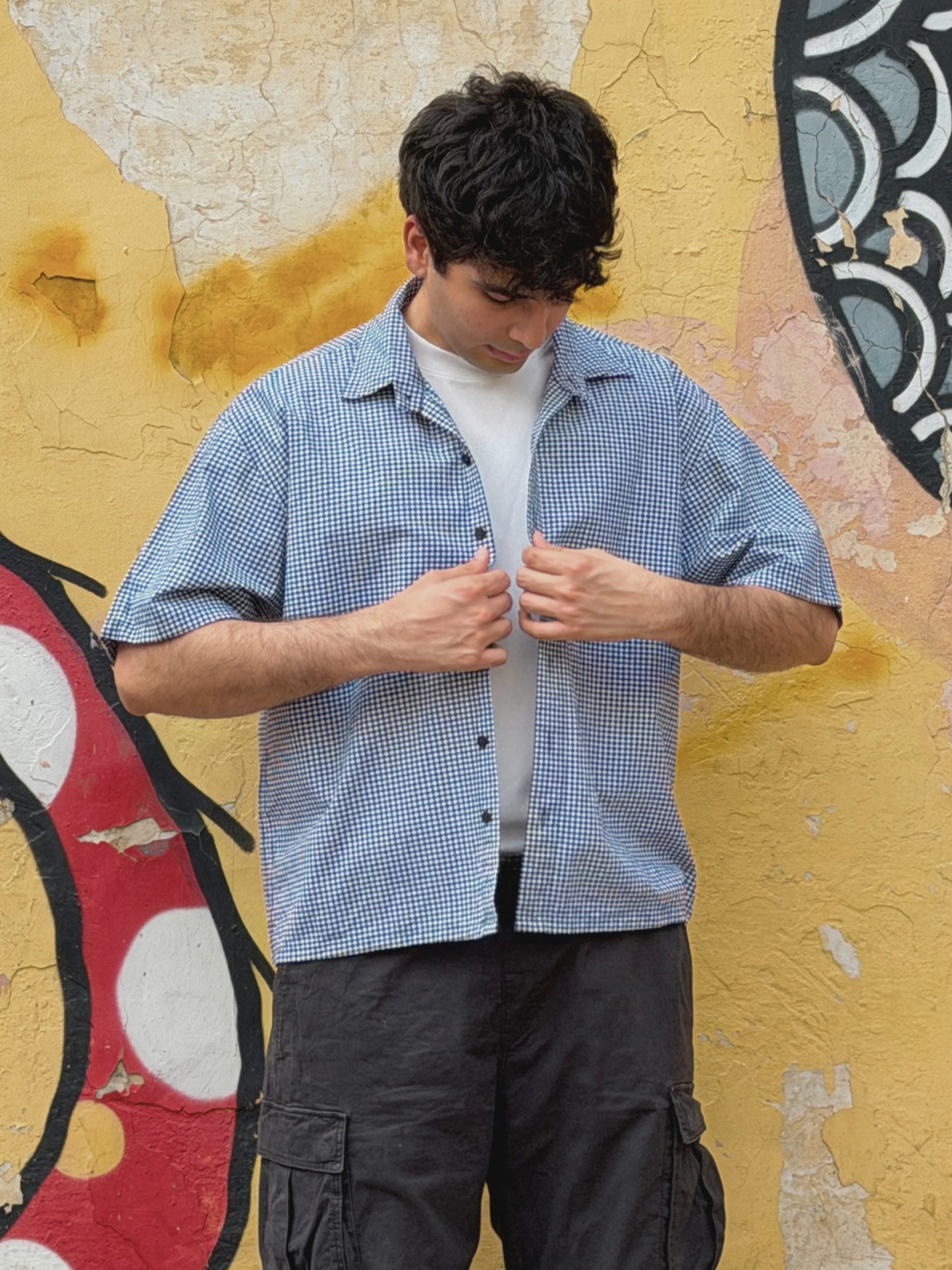 Man wearing classic london shirt over a white t-shirt, standing against a colorful wall.