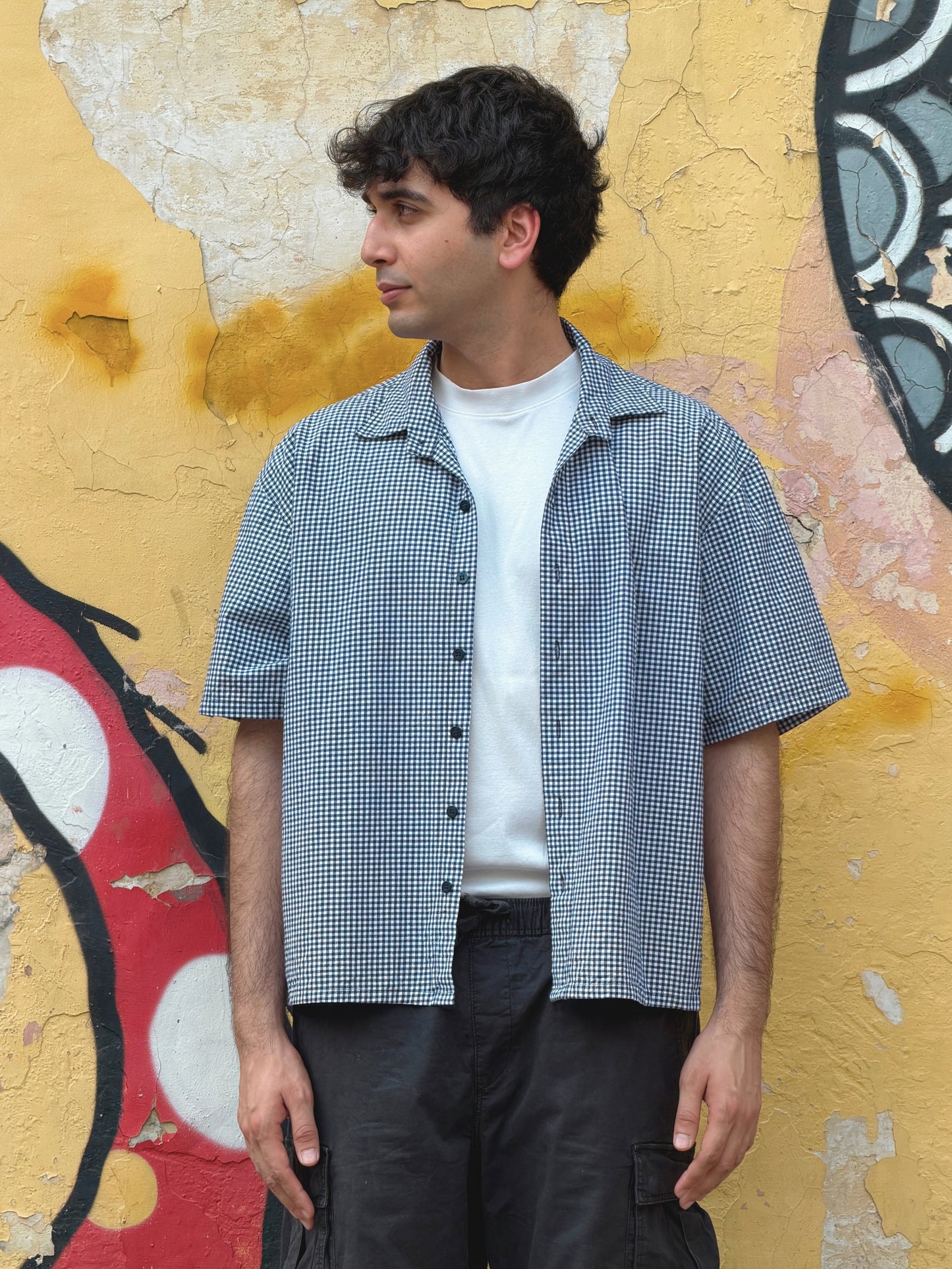 Man wearing the ikami london shirt over a white t-shirt against a graffiti-covered wall.